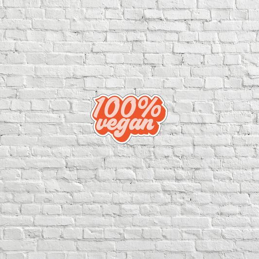 a white brick wall with a red sticker that says 100 % vegan